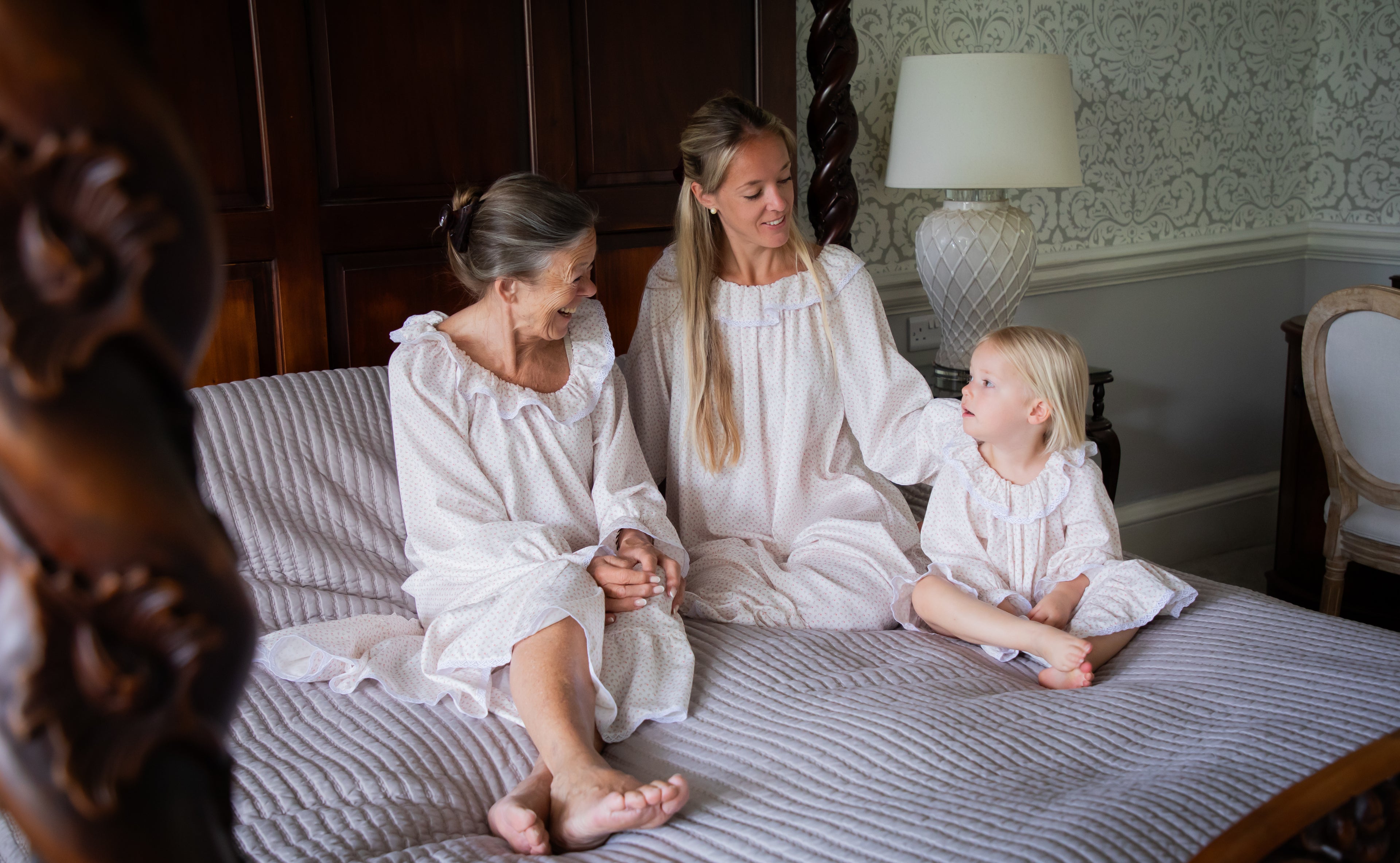 Grandmother, mother, and daughter wearing matching Harriet Jane London Briar Rose nighties in French cotton, sitting on a four-poster bed at Norwood Park